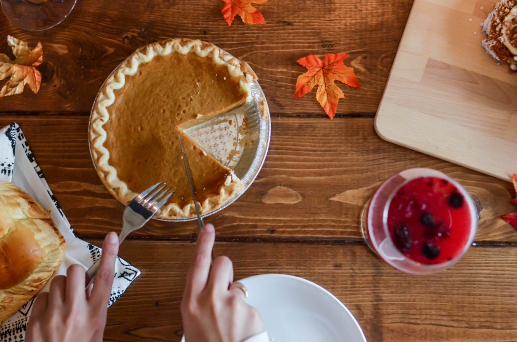 Picture of a person cutting into a pumpkin pie with leaves on the table