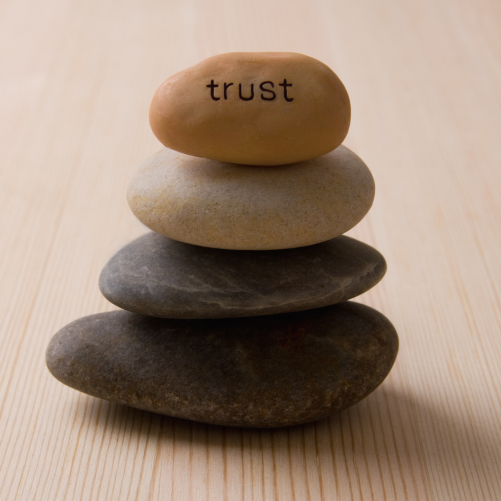 A photo of balancing rocks. The top rock says "trust"