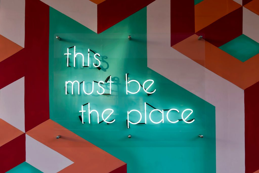 Neon sign reading “this must be the place” in a vibrant, modern workspace setting